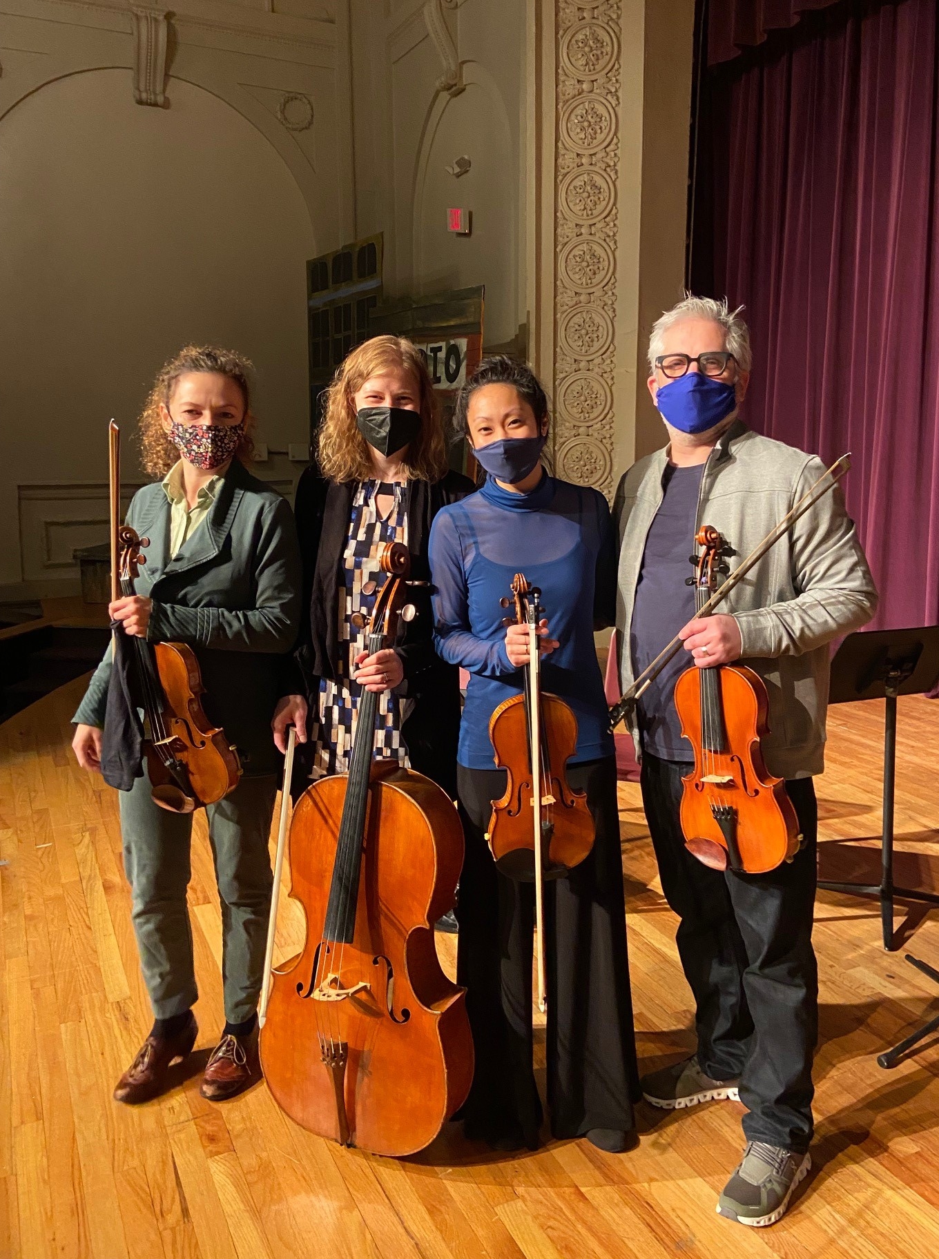 members of a string quartet holding their instruments on a school stage